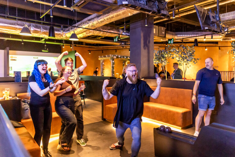 Group of friends cheering and raising their arms in a bowling alley lounge.