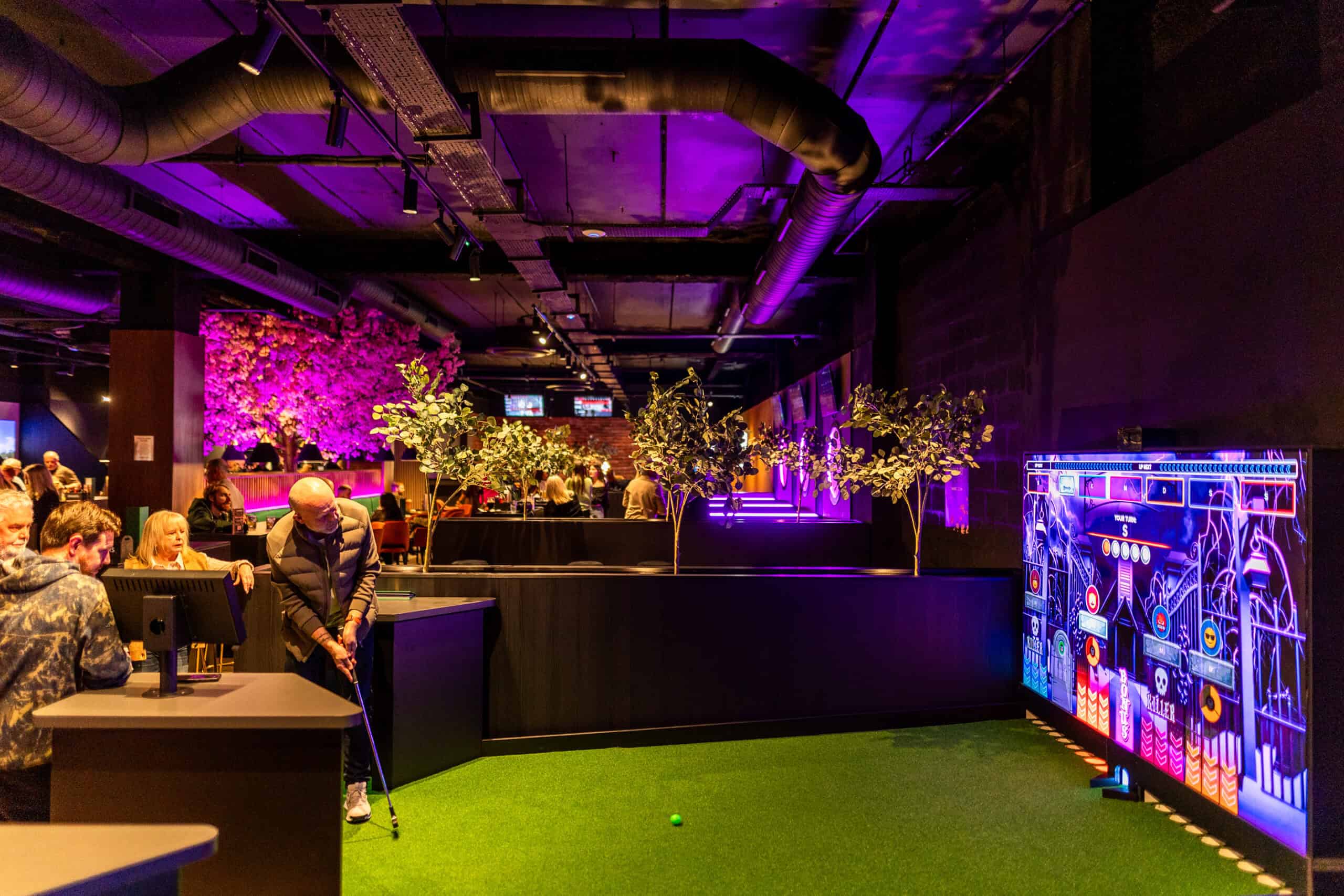 Players putting on the Interactive Golf green at Spinners with the LED scoring screen behind